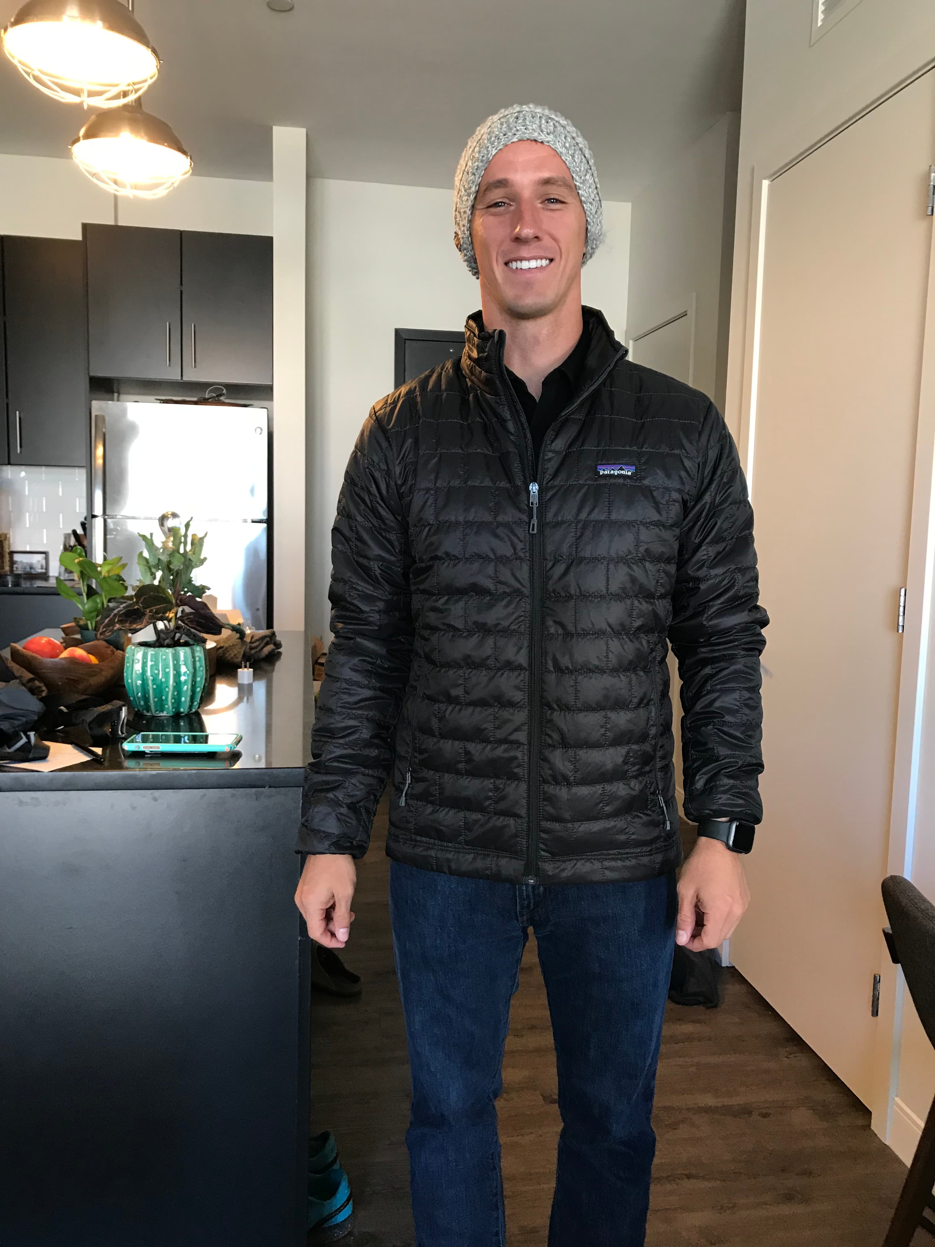 Dylan smiling in a black puffer jacket, jeans and a knit beanie, bundled up for a cold Asheville winter day