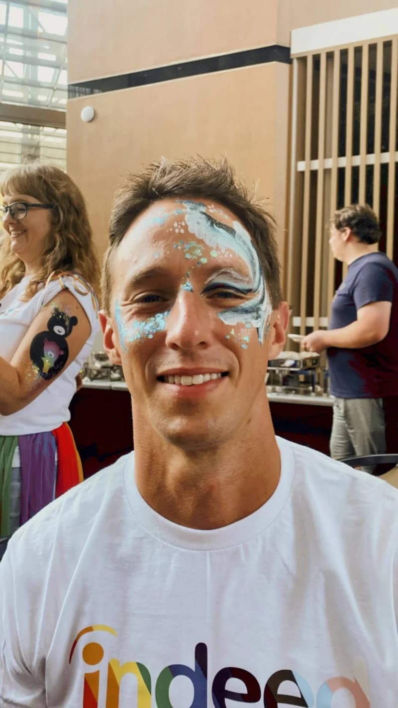 Dylan smiling with rainbow face paint at a Pride event in Asheville