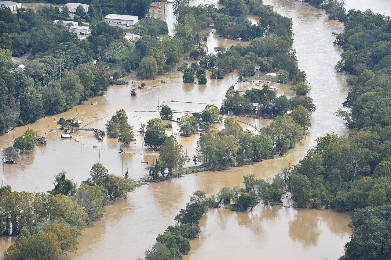 Aerial view of a brown, flooded river valley in western North Carolina after Hurricane Helene, with trees and buildings partly underwater