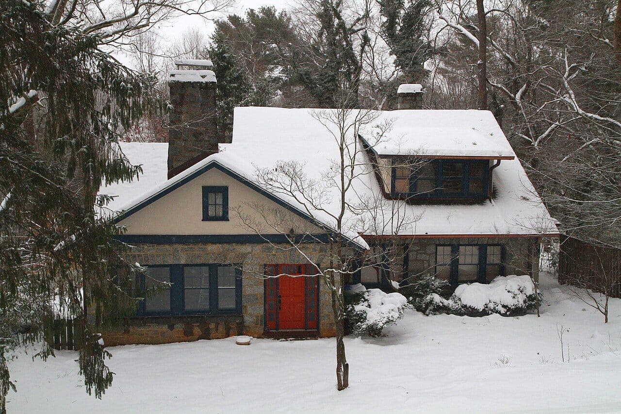 Asheville house with snow on the roof and yard, bare trees behind it