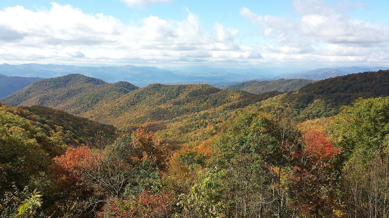 Rolling mountain ridges covered in orange, gold and green autumn leaves along the Blue Ridge Parkway south of Asheville