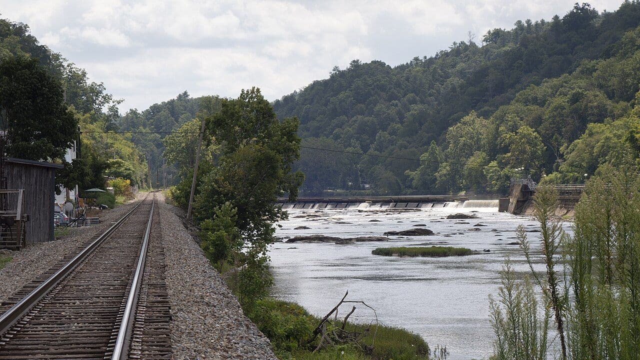 The wide French Broad River at Marshall with a low weir and a rail line running along the bank