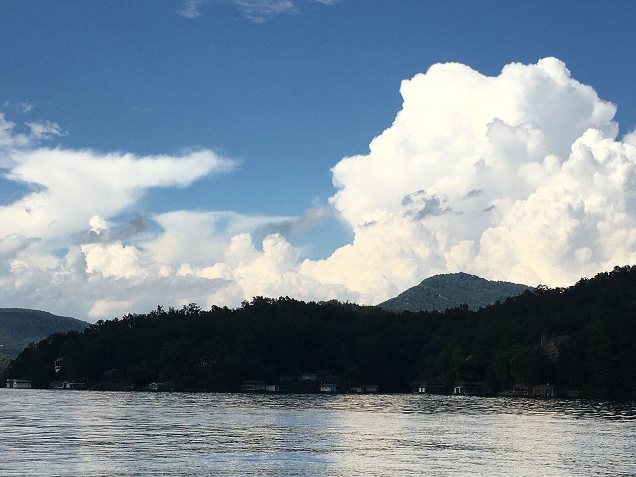 Lake Lure's calm water with wooded shoreline and mountains under a big summer cloud