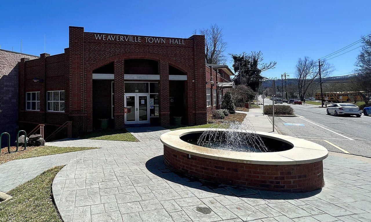 Red brick Weaverville Town Hall with a round fountain in the plaza out front