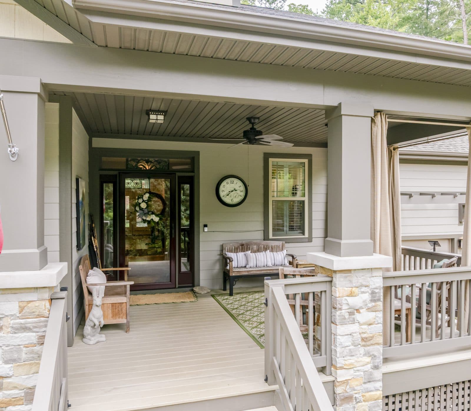 Covered front porch with stone columns, a bench, rocking chairs and a wreath on the door
