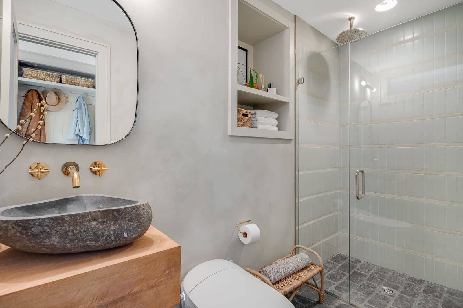 Bathroom with a glass-enclosed walk-in shower, stone vessel sink on a wood vanity and built-in shelves