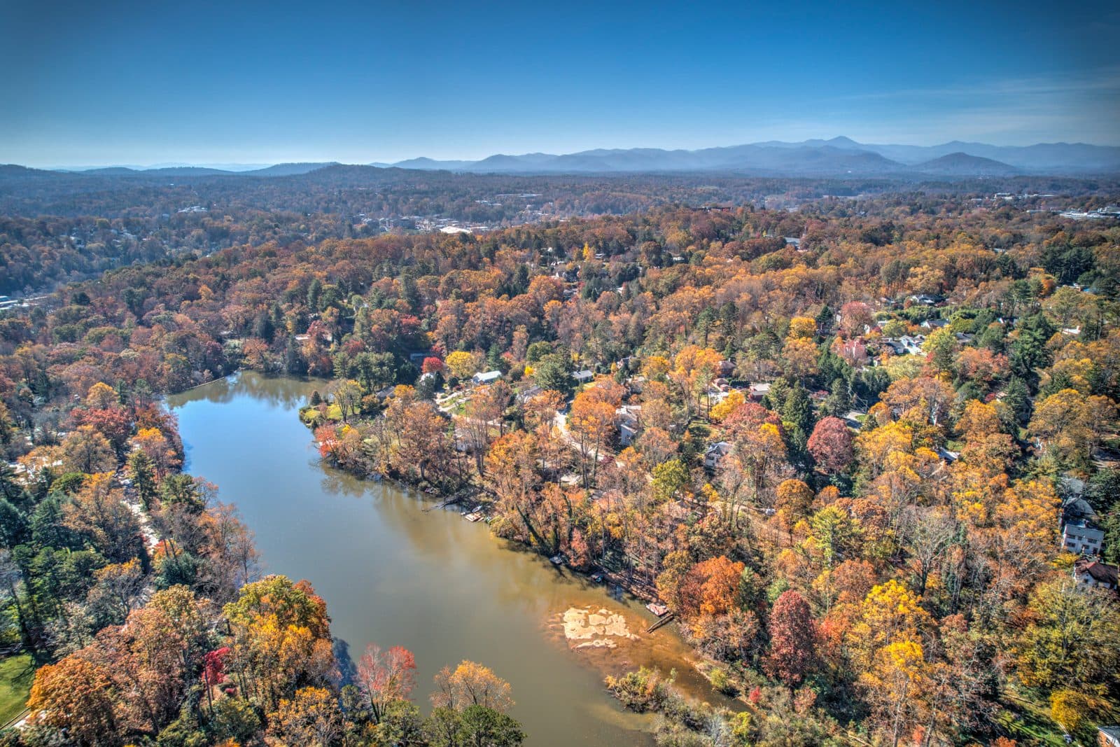 Aerial view of a lake surrounded by peak fall color with mountain ridges on the horizon, North Asheville