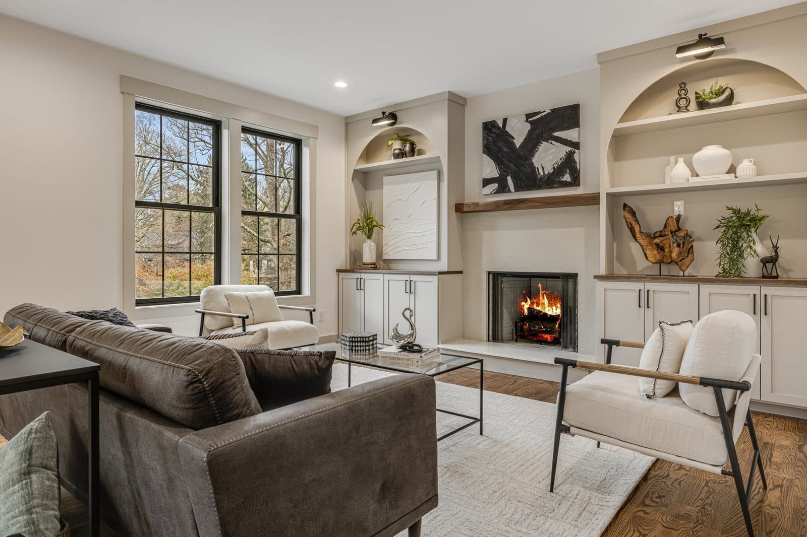 Living room with a fireplace, built-in arched shelves, big windows and a leather sofa