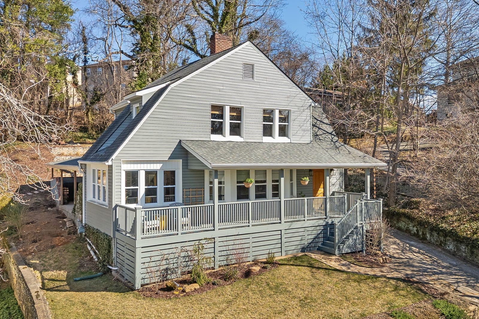Gray farmhouse-style home with a wraparound porch set on a wooded hillside