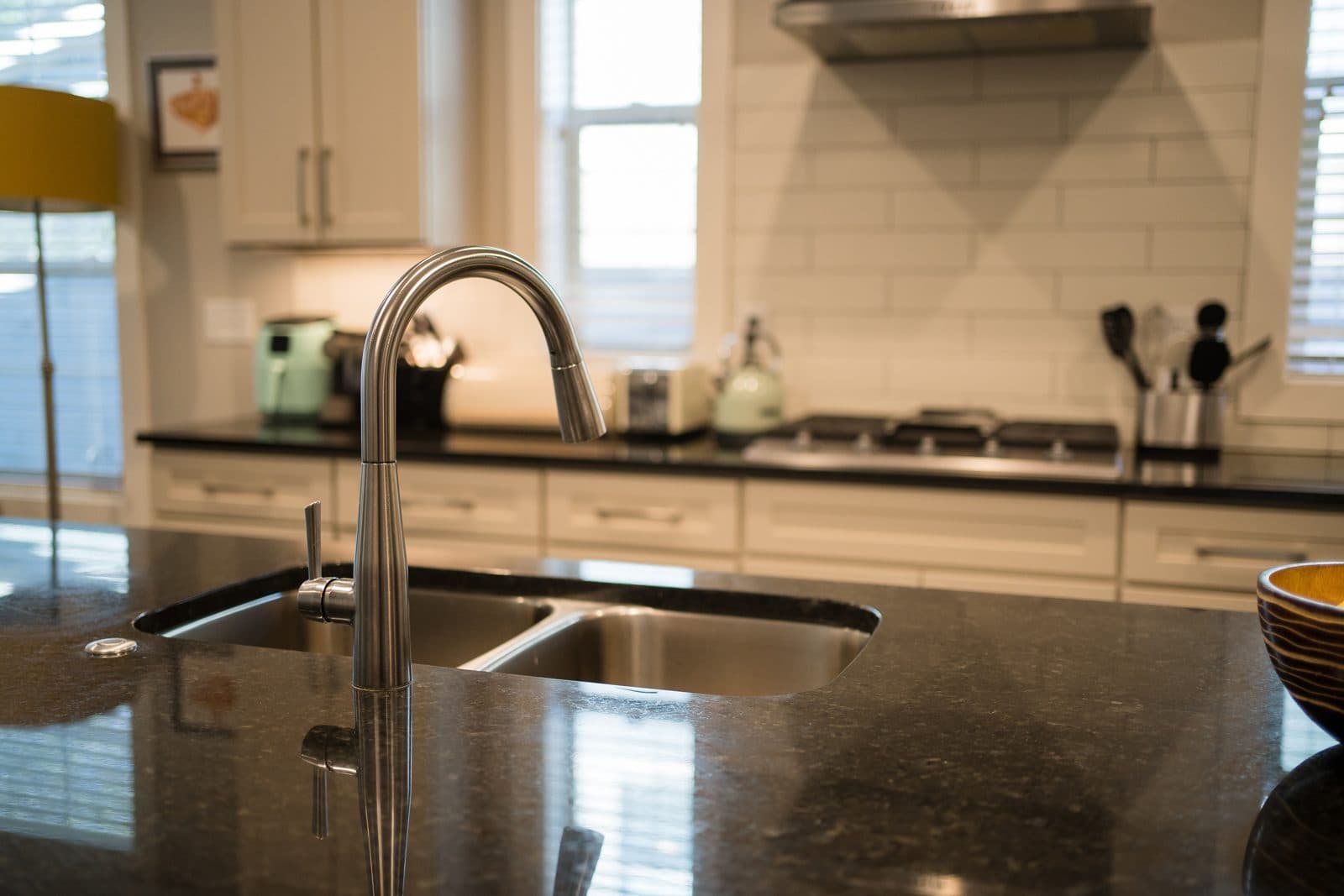 Kitchen detail with a black granite counter, gooseneck faucet, white subway tile and gas cooktop