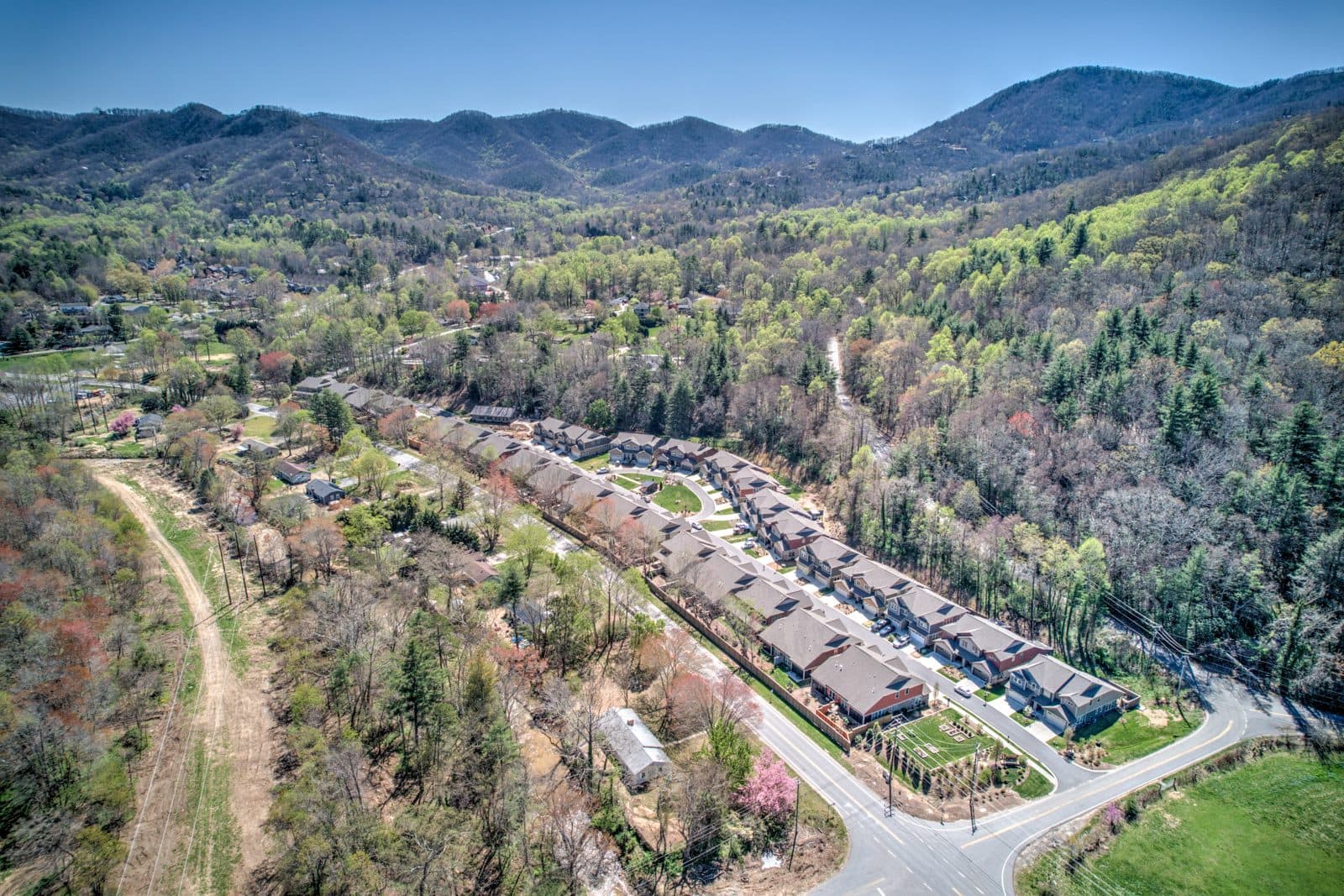 Aerial view of a row of townhomes along a curving road in a green mountain valley with ridges behind