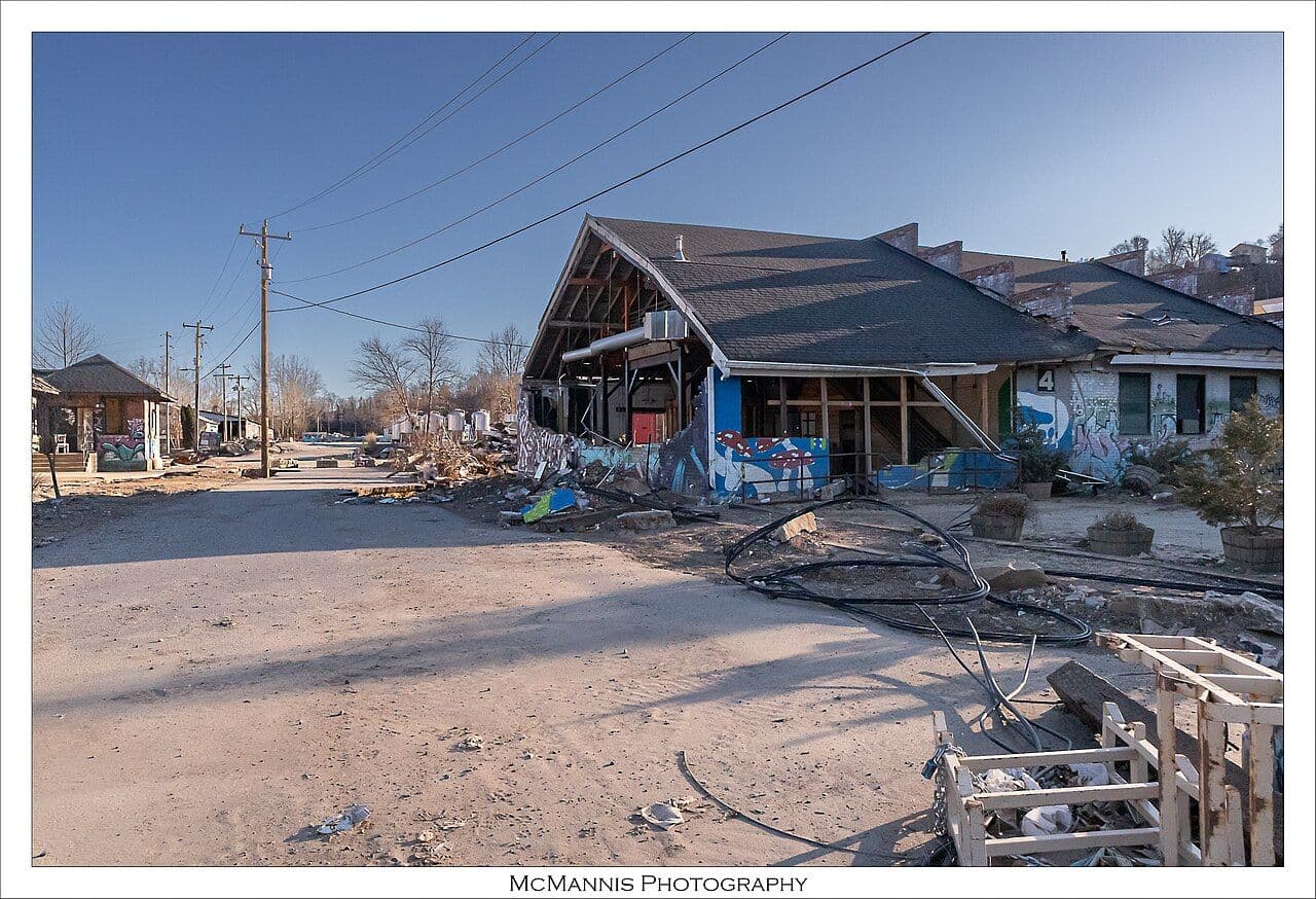 Damaged and boarded-up buildings along a dirt-covered street in Asheville's River Arts District, five months after Hurricane Helene